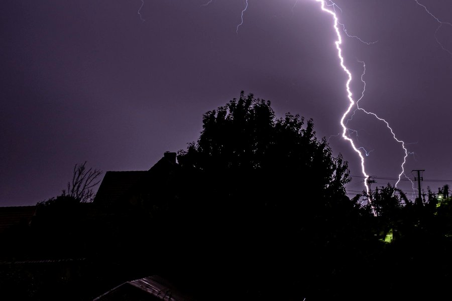 Lightning striking beside a power line above suburban rooftops at night